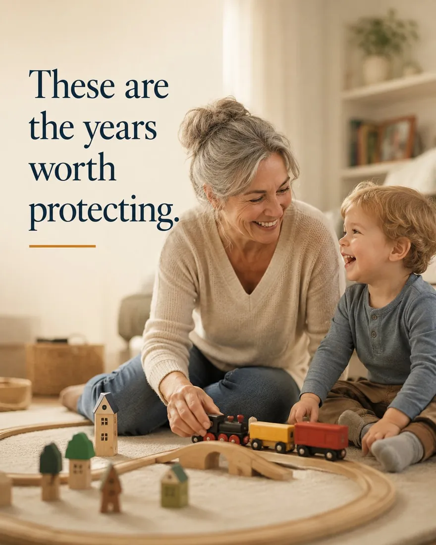 A grandmother and her young grandchild sitting on the floor together, building a wooden train set and laughing.